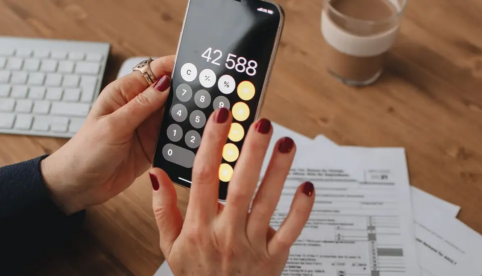 Manos usando la calculadora de un celular sobre formularios de impuestos